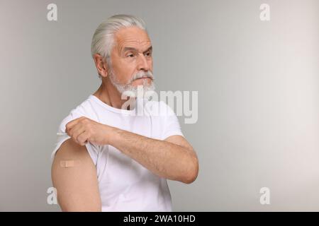 Homme âgé avec un bandage adhésif sur le bras après la vaccination sur fond gris clair, espace pour le texte Banque D'Images