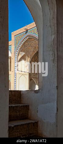 Vue panoramique verticale de la porte d'entrée principale de la mosquée Agha Bozorg du 18e siècle à travers un escalier étroit fendu. Kashan, Iran. Banque D'Images