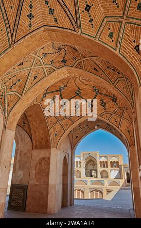 Vue de la porte d'entrée principale de la mosquée Agha Bozorg du 18e siècle à travers les arches du bâtiment principal. Kashan, Iran. Banque D'Images