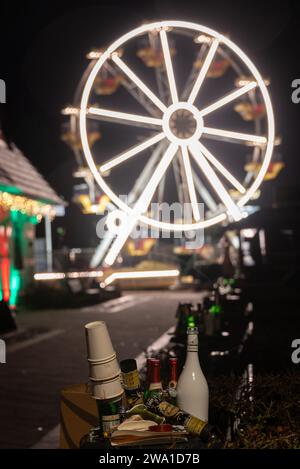 Zingst, Allemagne. 01 janvier 2024. Des bouteilles vides se dressent devant une grande roue illuminée sur la promenade de la plage après la Saint-Sylvestre. Crédit : Stephan Schulz/dpa-Zentralbild/dpa/Alamy Live News Banque D'Images