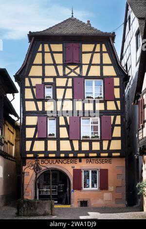 Maison à colombages traditionnelle colorée caractéristique avec une boulangerie et pâtisserie et un puits en face de l'entrée à Riquewihr en Alsace, Fran Banque D'Images