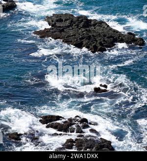 Mer bleue avec des vagues avec des chapeaux blancs. L'eau gonfle sauvagement et coule rapidement entre les roches noires dans l'eau Banque D'Images