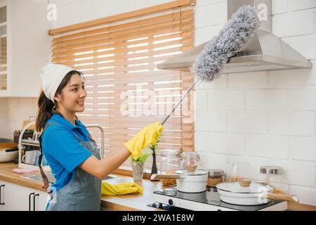 Asie femme femme de ménage dans des gants en caoutchouc et tablier nettoie la ventilation des poussières à la maison dans la cuisine. Hygiène Banque D'Images