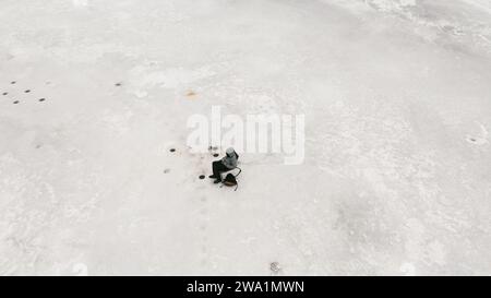 Garçon célibataire assis près du trou de pêche sur glace attendant une bouchée sur le lac gelé Banque D'Images