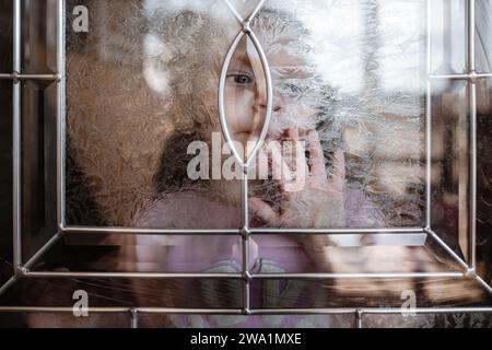 Enfant à la maison regardant à travers la fenêtre dans l'extérieur Banque D'Images