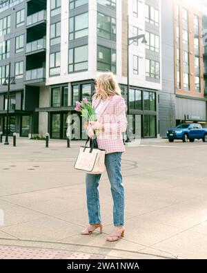 Femme élégante portant des tulipes dans la ville un jour de printemps Banque D'Images
