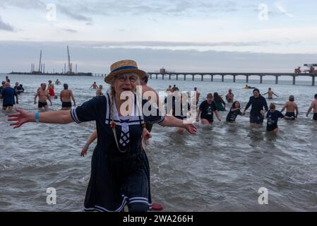 Prerow, Allemagne. 01 janvier 2024. Un nageur costumé grimpe joyeusement hors de l'eau froide à 5 degrés de la mer Baltique. Des centaines de vacanciers de nombreux États allemands ont une fois de plus participé à la traditionnelle baignade du nouvel an sur la péninsule de Fischland-Darß-Zingst. Crédit : Stephan Schulz/dpa/Alamy Live News Banque D'Images