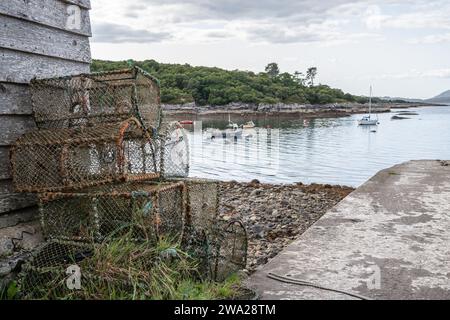 Pots de homard sur la voie de glissement à Glenuig avec des bateaux amarrés dans le Sound of Arisaig, Highlands, Écosse Banque D'Images