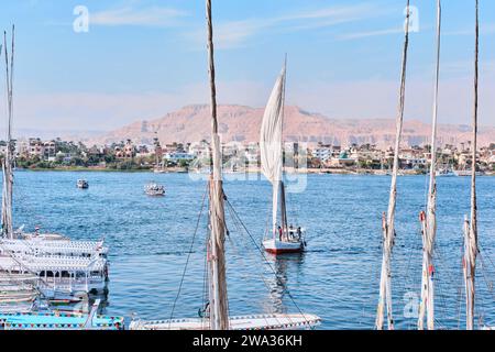Louxor, Égypte - décembre 26 2023 : feries à moteur traditionnelles et bateaux à voile Felucca amarrés le long du Nil Banque D'Images