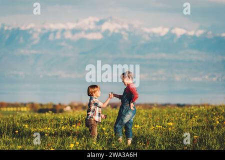 Deux enfants, petit frère et grande sœur, jouant ensemble en plein air dans des champs suisses avec vue sur le lac Léman et les montagnes françaises de haute-Savoie. Image t Banque D'Images