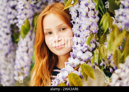 Gros plan portrait d'adorable fille aux cheveux rouges de 9-10 ans posant dans la Wisteria Banque D'Images