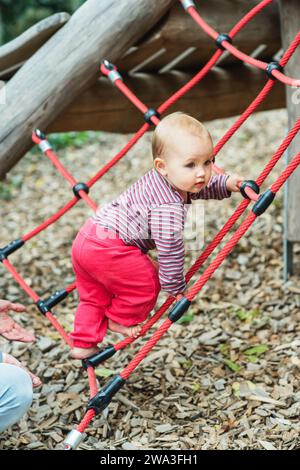 Adorable petite fille escaladant le filet sur le terrain de jeu. enfant de 9-12 mois s'amusant à l'extérieur Banque D'Images