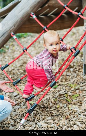 Adorable petite fille escaladant le filet sur le terrain de jeu. enfant de 9-12 mois s'amusant à l'extérieur Banque D'Images