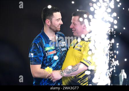 Luke Humphries célèbre sa victoire sur Dave Chisnall (à droite) le 14e jour du Championnat du monde de fléchettes Paddy Power à Alexandra Palace, Londres. Date de la photo : lundi 1 janvier 2024. Banque D'Images