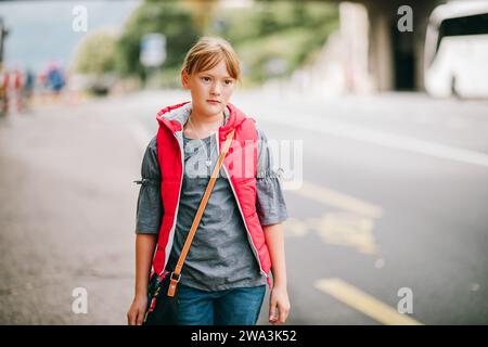 Portrait en plein air de petite fille élégante dans les rues de Genève, Suisse. Enfant portant une veste sans manches rouge vif Banque D'Images