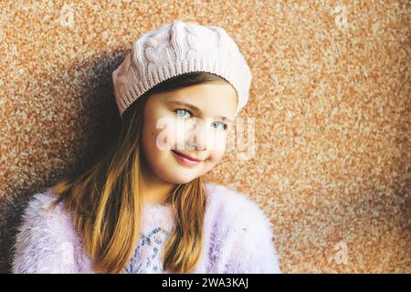 Gros plan portrait de mignonne petite fille de 9 ans avec les yeux bleus, portant un chapeau rose, debout sur fond brun Banque D'Images