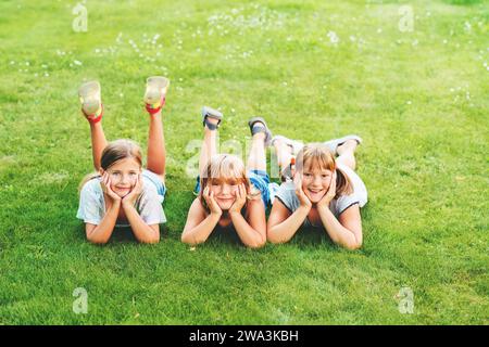 Groupe de trois enfants heureux couchés sur de l'herbe verte fraîche, regardant la caméra Banque D'Images