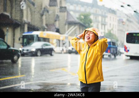 Mignon petit garçon jouant sous le, attrapant des gouttes d'eau par sa bouche, portant un imperméable jaune vif avec capuche. Image prise sur la place Saint-François, Banque D'Images