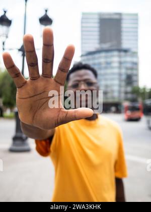 Jeune homme afro-américain insouciant étirant sa main vers la caméra dans une ville Banque D'Images