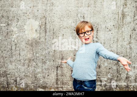 Portrait en plein air d'un mignon petit garçon portant des lunettes, pull bleu clair et jeans en denim Banque D'Images