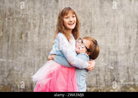 Portrait en plein air de deux enfants de mode drôles, tenant des boissons, portant des vêtements bleus et roses Banque D'Images