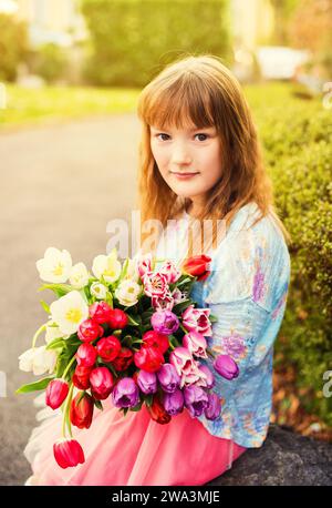 Portrait en plein air d'une petite fille douce avec un grand bouquet de tulipes colorées Banque D'Images