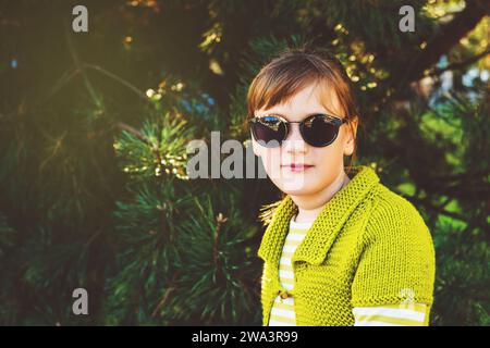 Portrait de mode d'une mignonne petite fille portant une veste en tricot vert vif et des lunettes de soleil Banque D'Images