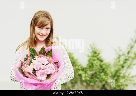 Gros plan portrait d'adorable fille enfant de cheveux bruns tenant grand bouquet de fleurs avec des roses, image de look de film Banque D'Images