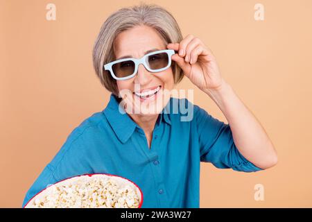 Photo de Toothy Beaming femme avec bob Hair Dressed bleu chemise touch lunettes 3d tiennent le pop-corn au cinéma isolé sur fond de couleur pastel Banque D'Images