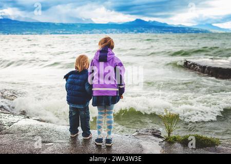 Groupe de deux petits enfants jouant au bord du lac Léman par une journée très venteuse, Suisse Banque D'Images