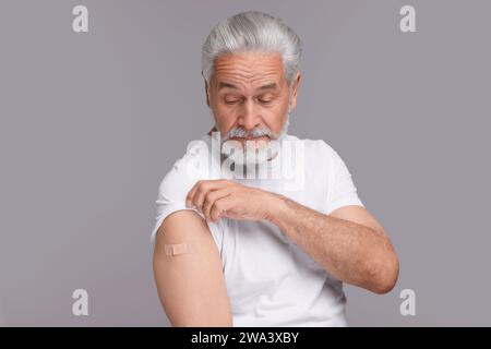 Homme âgé avec un bandage adhésif sur le bras après vaccination sur fond gris clair Banque D'Images