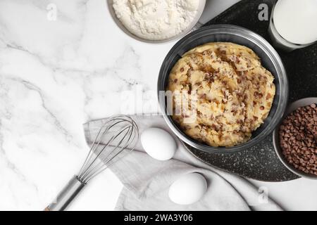 Pâte à biscuits aux pépites de chocolat dans un bol et ingrédients sur une table en marbre blanc, mise à plat. Espace pour le texte Banque D'Images