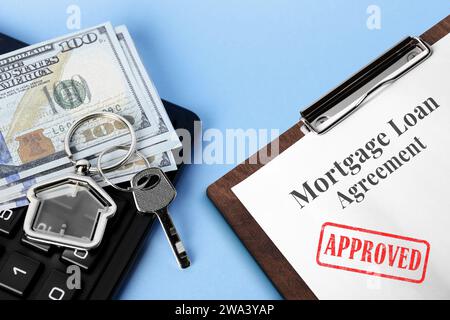 Accord de prêt hypothécaire avec timbre approuvé, clé de maison, argent et calculatrice sur fond bleu clair, closeup Banque D'Images