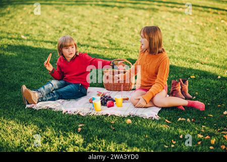 Les enfants mangent des collations à l'extérieur. Enfants se reposant dans le parc sur une belle journée ensoleillée assis sur la couverture Banque D'Images