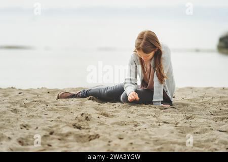 Adorable petite fille de 8-9 ans jouant au bord du lac, portant un pantalon gris et un long cardigan Banque D'Images