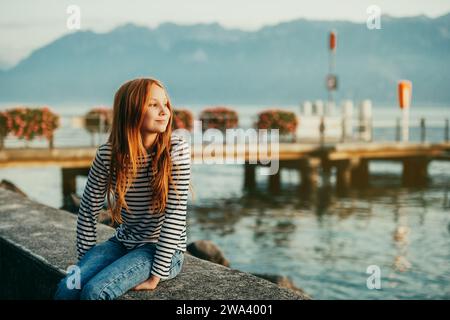 Mignonne petite fille rousse reposant au bord du lac Léman au coucher du soleil, image prise à Lausanne, Suisse Banque D'Images