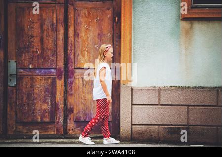Portrait de mode en plein air d'une fille de 8-9 ans marchant dans la rue, portant un pantalon polkadot et un tee-shirt blanc, image tonique Banque D'Images