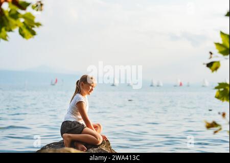 Mignonne petite fille reposant au bord du lac Genève au coucher du soleil Banque D'Images