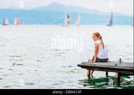 Mignon petite fille d'enfant reposant au bord du lac, assis sur la jetée, éclaboussant de l'eau avec ses pieds, vue arrière Banque D'Images