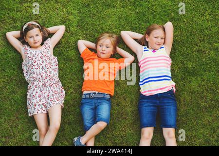 Enfants heureux s'amusant à l'extérieur. Enfants jouant dans le parc d'été. Petit garçon et deux filles allongées sur de l'herbe verte fraîche Banque D'Images