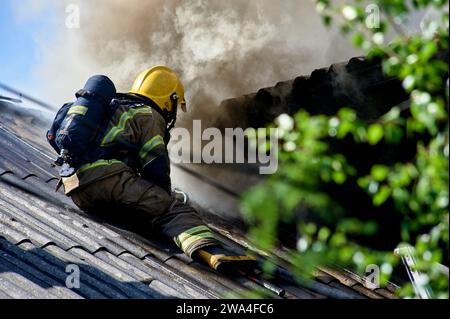 Un pompier sur le toit d'une maison éteint un incendie Banque D'Images