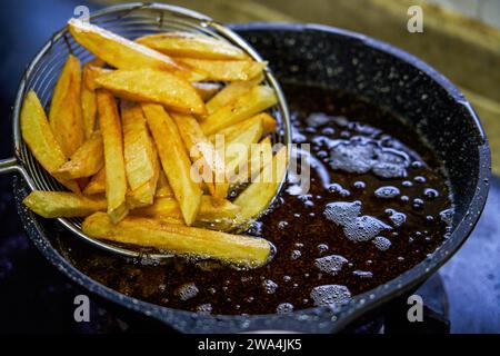 Un chef frit des frites dans une poêle Banque D'Images