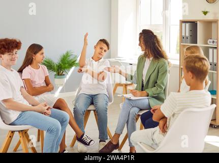 Écolier, assis en cercle avec ses camarades de classe, lève la main pour répondre à la question du professeur. Banque D'Images