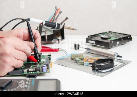 Gros plan des mains d'un technicien dans un atelier. Le réparateur utilise un multimètre pour mesurer les paramètres d'un appareil électronique sur une table. Banque D'Images