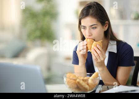 Découragé femme anxieuse mangeant la boulangerie essayant de soulager l'anxiété à la maison Banque D'Images