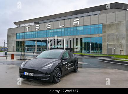 02 janvier 2024, Brandenburg, Grünheide : un véhicule électrique Tesla Model y se dresse devant la Tesla Gigafactory Berlin-Brandenburg. Le constructeur de voitures électriques américain Tesla veut promouvoir l'expansion prévue du site de l'usine avec un «Road show». La série de cinq événements d'information pour les résidents locaux a commencé mardi à Grünheide dans le Brandebourg. L'usine automobile est située dans la municipalité. Tesla veut construire un dépôt de fret, des entrepôts et une garderie sur un site adjacent. Photo : Patrick Pleul/dpa Banque D'Images