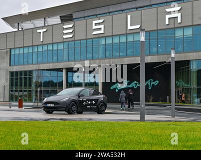 02 janvier 2024, Brandenburg, Grünheide : un véhicule électrique Tesla Model y se dresse devant la Tesla Gigafactory Berlin-Brandenburg. Le constructeur de voitures électriques américain Tesla veut promouvoir l'expansion prévue du site de l'usine avec un «Road show». La série de cinq événements d'information pour les résidents locaux a commencé mardi à Grünheide dans le Brandebourg. L'usine automobile est située dans la municipalité. Tesla veut construire un dépôt de fret, des entrepôts et une garderie sur un site adjacent. Photo : Patrick Pleul/dpa Banque D'Images