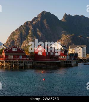 Le petit village de Henningsvaer sur la côte sud des Lofoten, sur une soirée d'été avec la lumière du soleil, des maisons colorées rouges et des sommets de montagne. Banque D'Images