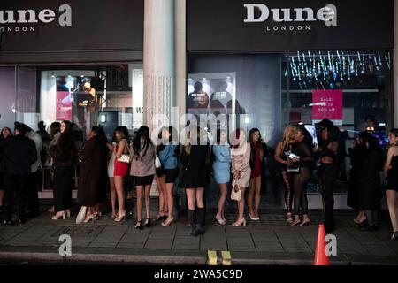 Les jeunes femmes font la queue devant une boîte de nuit lors d'une soirée du nouvel an humide en mottes dans le quartier du West End de la capitale, Londres, Angleterre, Royaume-Uni. Banque D'Images