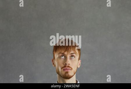 Jeune homme regardant vers le haut, rêvant, pensant ou imaginant quelque chose sur fond d'espace de copie Banque D'Images
